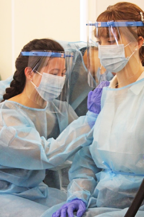 Two women in protective gear. One is giving the other a shot.