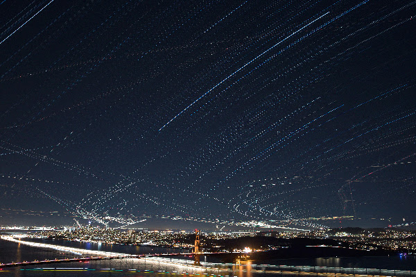 AlieNation art exhibit photograph showing a nighttime cityscape with light trails above a brightly lit bridge and city.