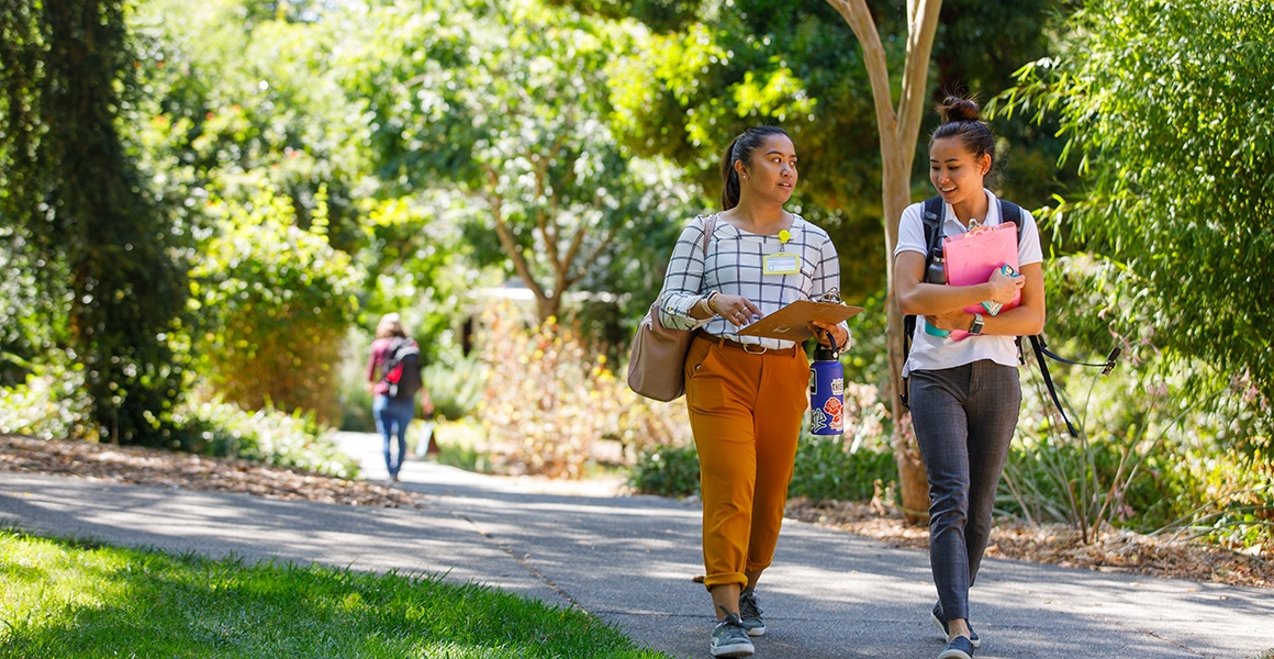 two students walk down a path with their books and backpacks on the Dominican campus