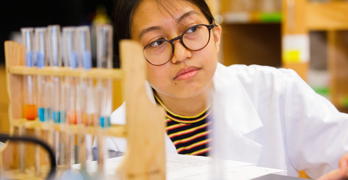 girl in lab coat next to test tubes in a lab