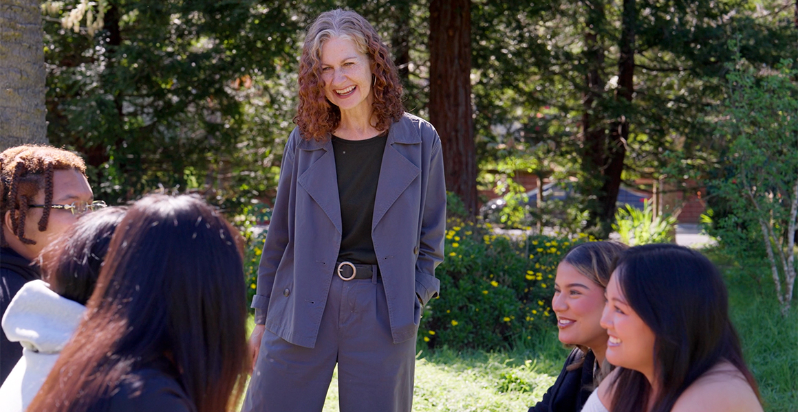 Dominican University's President Nicola Pitchford smiling and talking to students outdoors on the Dominican campus.
