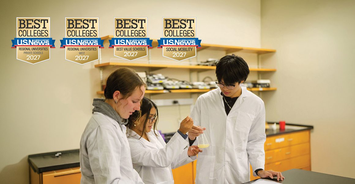 Three students in white lab coats conduct a science experiment in a classroom lab, with Best Colleges U.S. News awards displayed above.