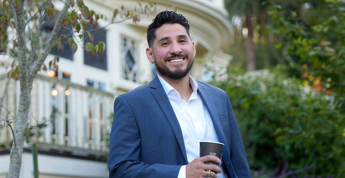 graduate student in a suit holding a coffee smiling