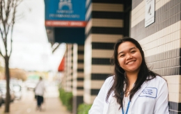 Smiling female student in a lab coat stands in front of the Kaiser Permanente building