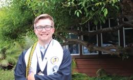 Jake Quast, Dominican University of California Class of 2019 Outstanding Student smiles at the camera in graduation garb