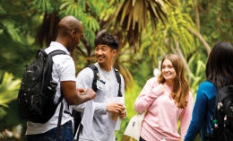 Two male and two female Dominican students standing outside with their backpacks; green leaves in the background