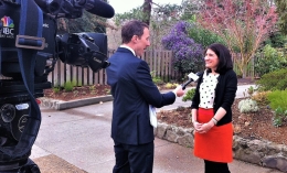 Photo of Alison Howard being interviewed by TV reporter/cameraman years ago for story about first 100 days of Biden Administration