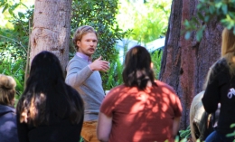 Photo of psychology professor Dr. Ben Rosenberg teaching outdoor class at Dominican with students sitting on tree stumps with backs to camera