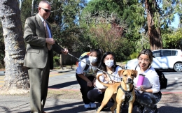Photo of Prof. Brad Van Alstyne's new dog Zizi being petted by three kneeling DU students