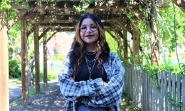 Photo of Salmaa Hussain with arms folded standing and smiling under ivy-covered terrace on campus