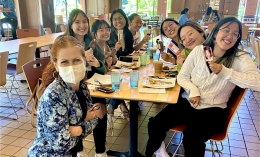 Photo of Dominican President Nicola Pitchford kneeling in front of table in Caleruega Dining Hall with seven students sitting around it smiling