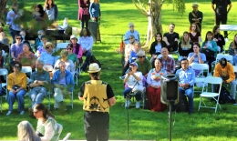 Photo from behind and above the stage of speaker and crowd for Indigenous Peoples' Day ceremony on Anne Hathaway Lawn in 2022