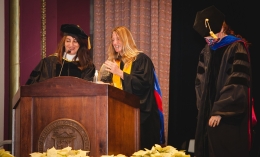 Photo of Lynn Sondag (center) in regalia receiving Fink Faculty Award at podium during 2022 Fall Commencement ceremony flanked by Mojgan Bermand (left) and Dominican President Nicola Pitchford