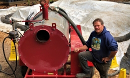 Photo of NORS-DUC's Vernon Huffman in blue hoodie posing with right knee propped on bumper of red steamer