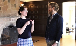 Photo of Elana Antolin-Wilczek (left) wearing dark top and blue checkered shirt, conversing with Dr. Benjamin Rosenberg with stone fireplace over Elana's right shoulder