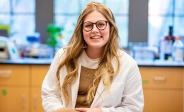 Photo of Biological Sciences graduate student smiling and wearing white lab coat in laboratory classroom