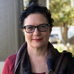 Jan VanStavern, a teacher with short brown hair and glasses, smiles in a scarf outdoors.