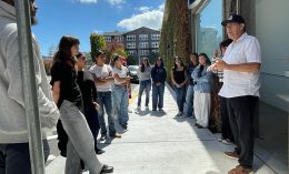 Service-learning students from Dominican University of California gather outside and listen to a man speaking.