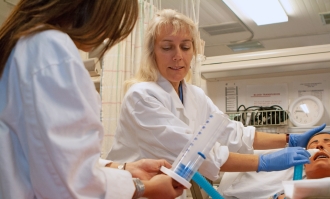Photo of nursing professor Dr. Luanne Linnard-Palmer (center) examining a dummy patient in a simulation lab on campus