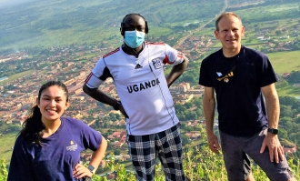 Photo of Professor Roland Cooper (right) standing on hillside above a Ugandan village with Martin Okitwi and Dominican alumna Frida Ceja '17 (kneeling left)