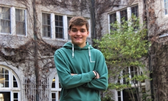 Photo of ACS student Dylan Player wearing green Spotify hoodie arms folded posing outside Fanjeaux Hall