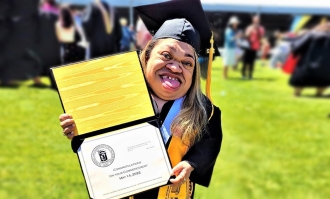 Photo of Patricia Ramos '22, in black cap and gown, posing holding her diploma she received at Dominican Commencement in May 2022