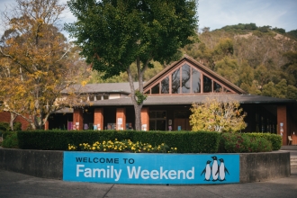 Photo of blue Family Weekend banner attached to flower wall in middle of Caleruega Dining Hall Plaza