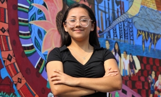 Smiling Britney Gutierrez Calderon wearing black top with arms folded standing and posing in front of colorful mural at Canal Alliance