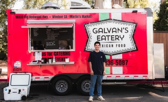 Photo of MBA graduate Ivan Galvan in dark clothing standing in front of red Galvan Eatery taco truck parked in Conlan Center lot