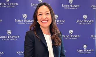 Photo of Ashley Ramirez wearing dark jacket and standing in front of purple banner for Johns Hopkins University