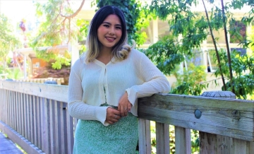 Photo of Sulgi Kim smiling and posing while leaning against foot bridge on campus