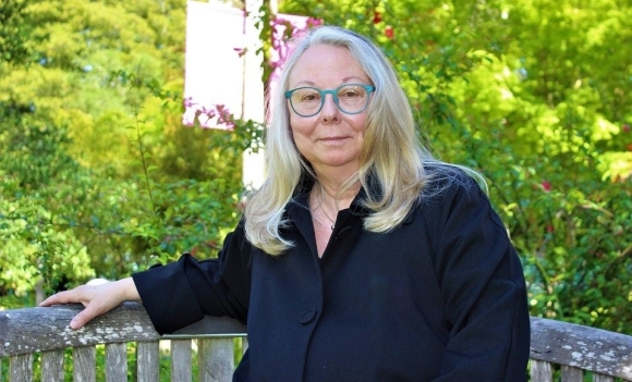 Photo of 69-year-old ADC student Renee Dunn, smiling wearing dark top and sitting on wooden bench on campus