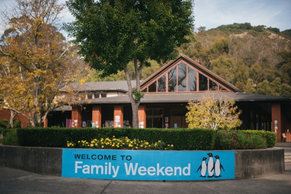 Photo of blue Family Weekend banner attached to flower wall in middle of Caleruega Dining Hall Plaza