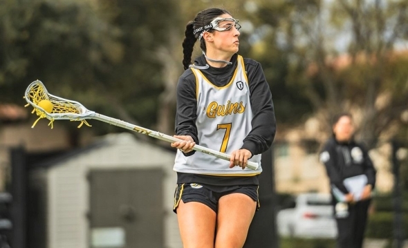 Photo of Dominican women's lacrosse player Taylor Pieri, wearing white number 7 jersey, looking downfield left while holding her lacrosse stick with both hands angled to her right.