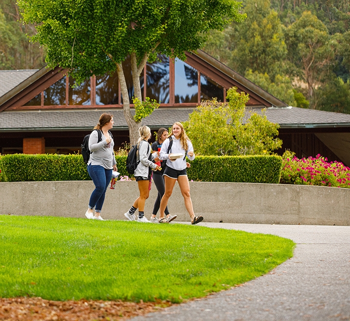 A group of students walks by Caleruega Dining Hall on the Dominican University of California campus.