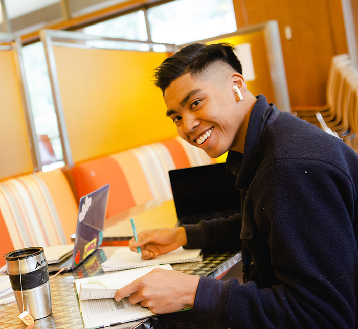 A young man smiles as he studies and takes notes.