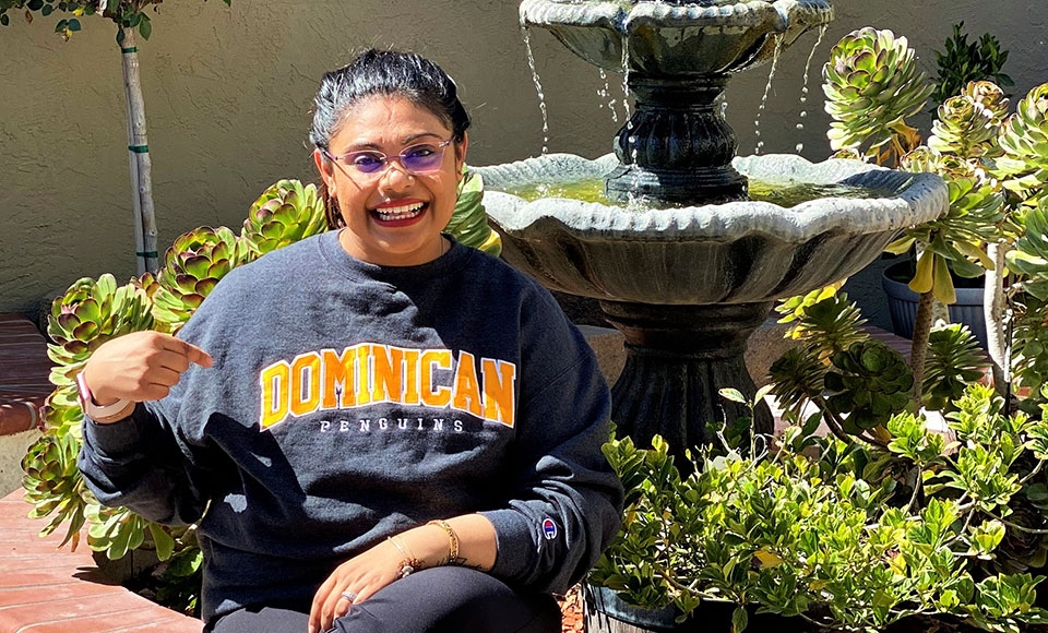 female student divya mistry wearing a Dominican sweatshirt sitting outside by a fountain.