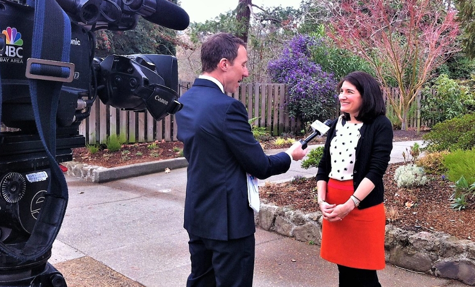 Photo of Alison Howard being interviewed by TV reporter/cameraman years ago for story about first 100 days of Biden Administration