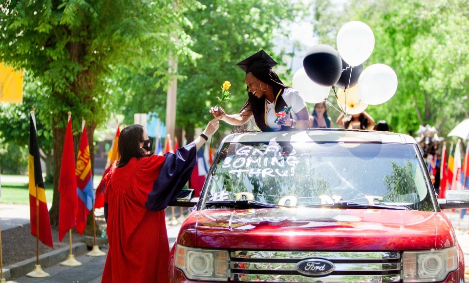 Photo of President Marcy handing yellow rose to graduate standing through sunroof at drive-thru celebration on campus