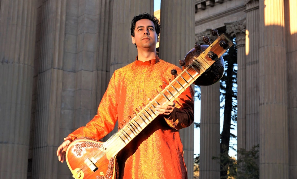 Photo of alum Arjun Verma posing with sitar in front of Palace Of The Fine Arts