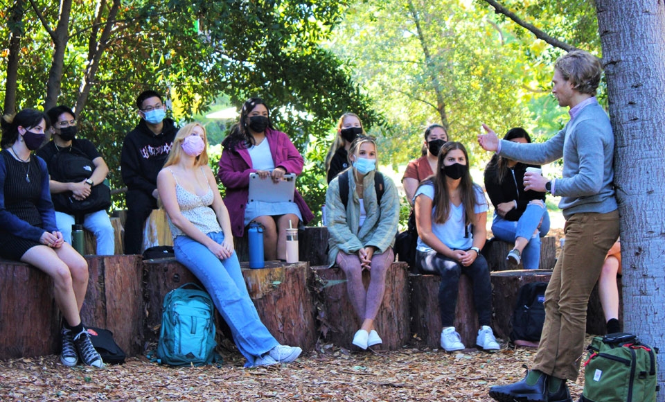 Photo of Dr. Ben Rosenberg talking to his masked psychology class students sitting in an outdoor classroom