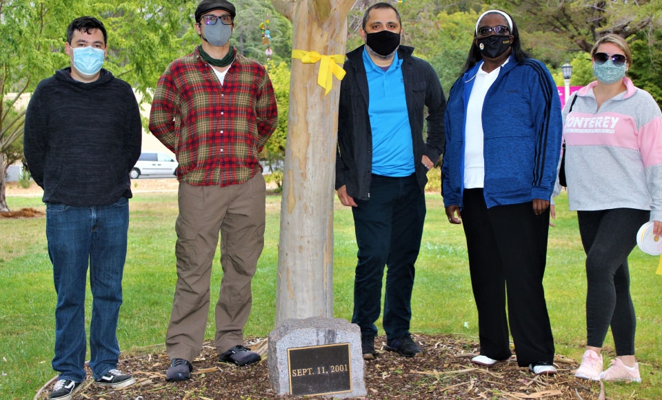 Photo of five Dominican veterans posing in front of 9/11 memorial tree with yellow ribbon attached on Anne Hathaway Lawn on campus