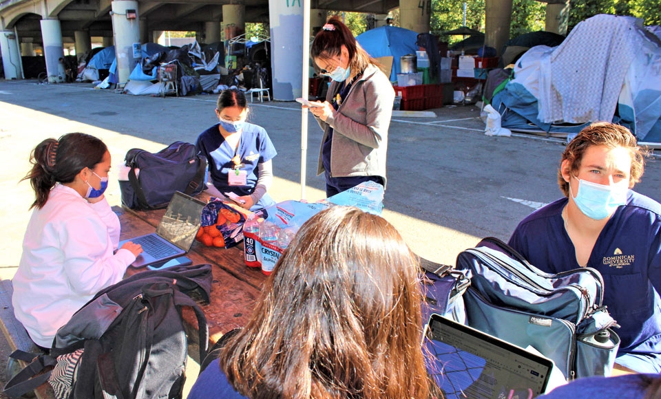 Nursing students sitting in an assessment tent next to homeless encampment