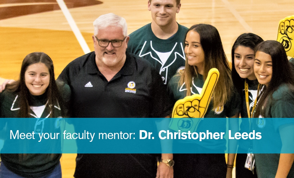 Photo of Dr. Christopher Leeds smiling and standing with a half dozen student-athletes on the basketball court on Academic Night in Conlan Center