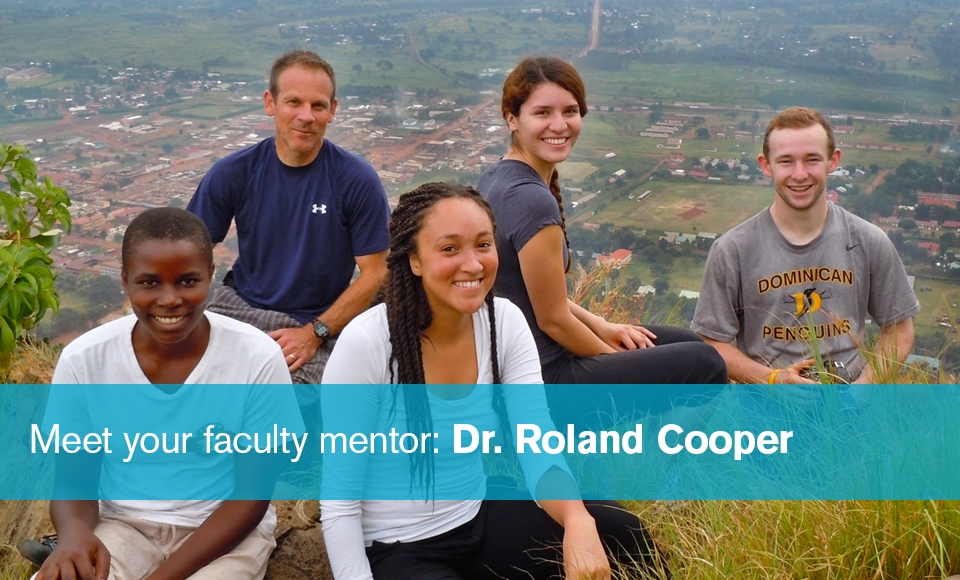 Photo of Dr. Roland Cooper (back row, far left) sitting with four other malaria research students on top of a hill overlooking a village in Uganda