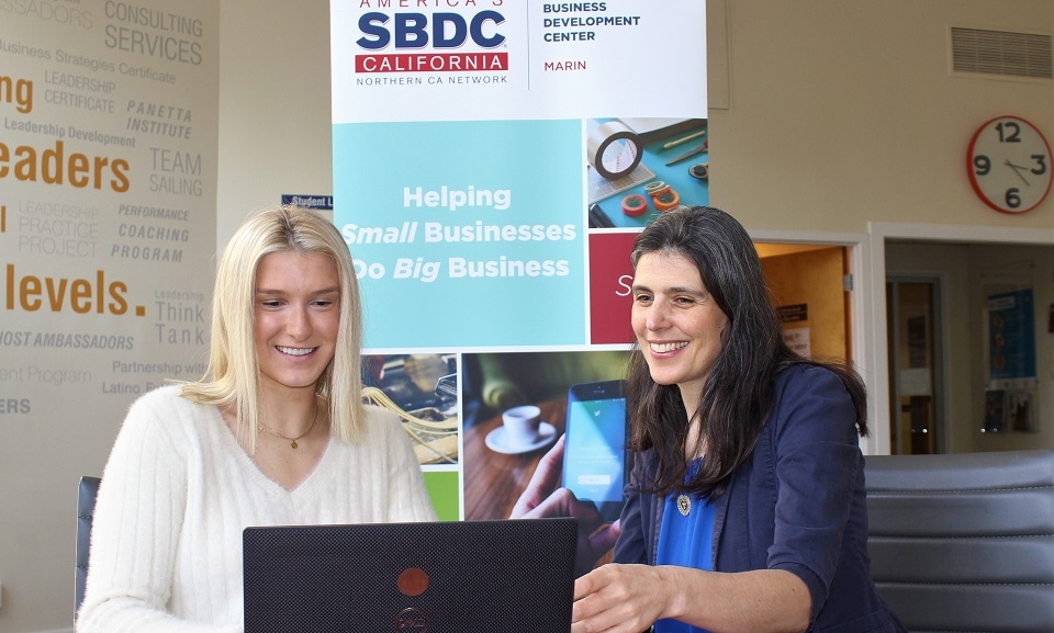Photo of MBA student and Marin Small Business Development Center intern Riley Friauf (left) sitting and typing on laptop computer with SBDC Director Miriam Hope Kanell sitting next to her
