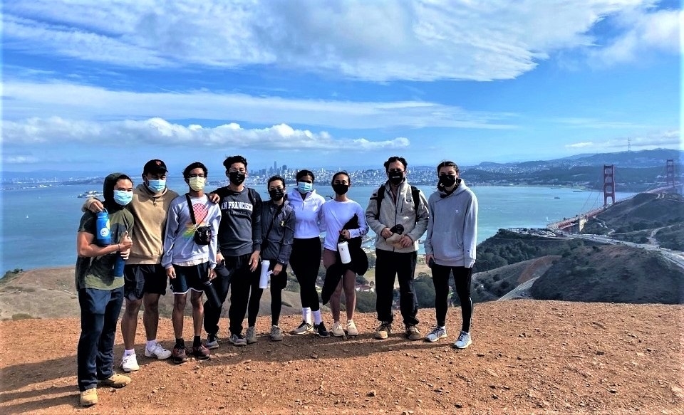 Group photo of nine participants in Dominican Rec Sports' Sunday Hike posing in Marin Headlands above Golden Gate Bridge